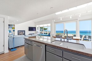 A modern kitchen with a large island, a dining area with a view of the sea, and a living room with a fireplace. - Tides In - Monterey Beach House - Oceanfront, Walk to Fisherman's Wharf (Monterey)
