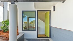 Una entrada moderna con puerta de vidrio, una jardinera de concreto con planta y una escalera visible que conduce al interior.