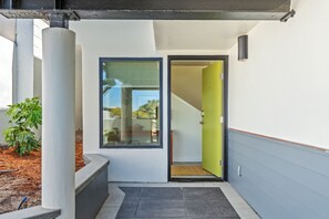 Una entrada moderna con puerta de vidrio, una jardinera de concreto con planta y una escalera visible que conduce al interior.