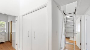 Un pasillo con un armario blanco, suelo de madera y una escalera metálica.
