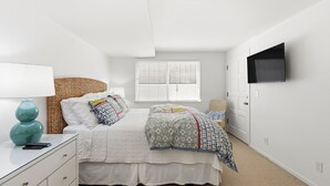 Un dormitorio con cama, mesita de noche, lámpara y televisor montado en la pared.