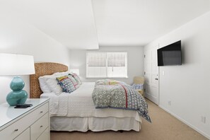 Un dormitorio con cama, mesita de noche, lámpara y televisor montado en la pared.