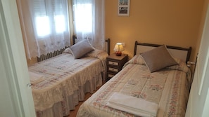 Une chambre avec deux lits simples, chacun agrémenté d’une literie à motifs floraux et d’une table de chevet avec une lampe.