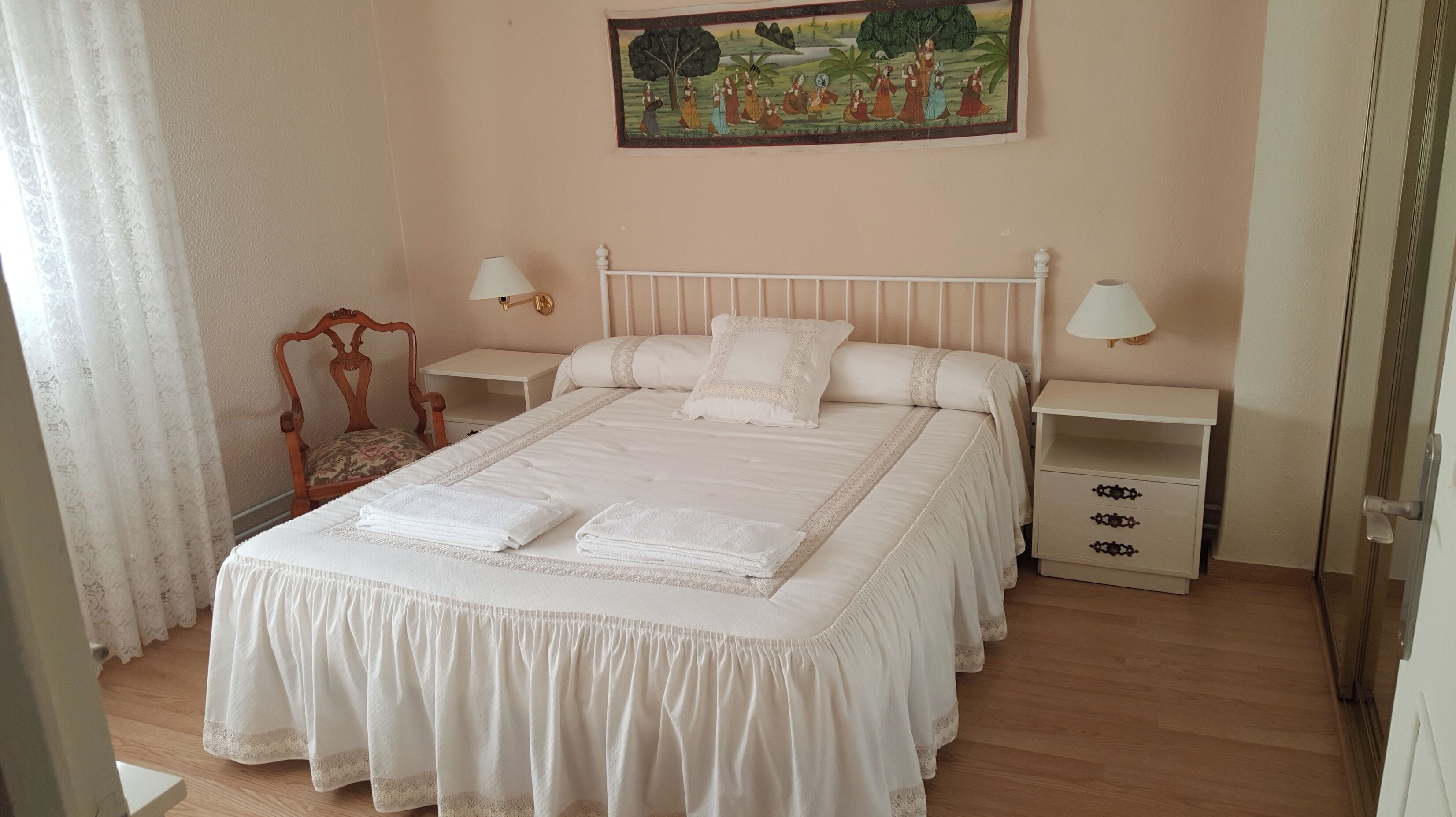 A neatly arranged bedroom with a large bed, two bedside tables, a chair, and a painting on the wall.