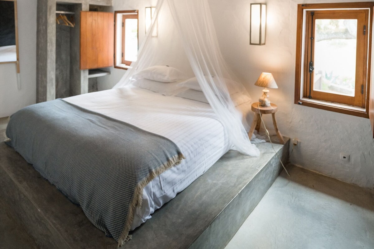 A bedroom with a bed, a bedside table with a lamp, a window, and a wardrobe.