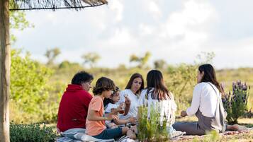 A group of people sitting on a blanket outdoors, with a thatched structure nearby.