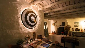 A cozy reading nook with a fireplace, books, and a decorative wall light. - Monte Gois Country House e Spa (Almodôvar)