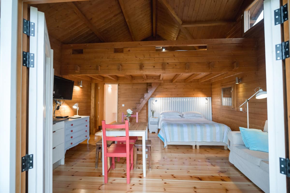 A wooden cabin interior with a dining area, a bed, and a sofa.