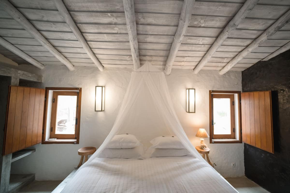A bedroom with a canopy bed, wooden walls, and two windows with wooden shutters.