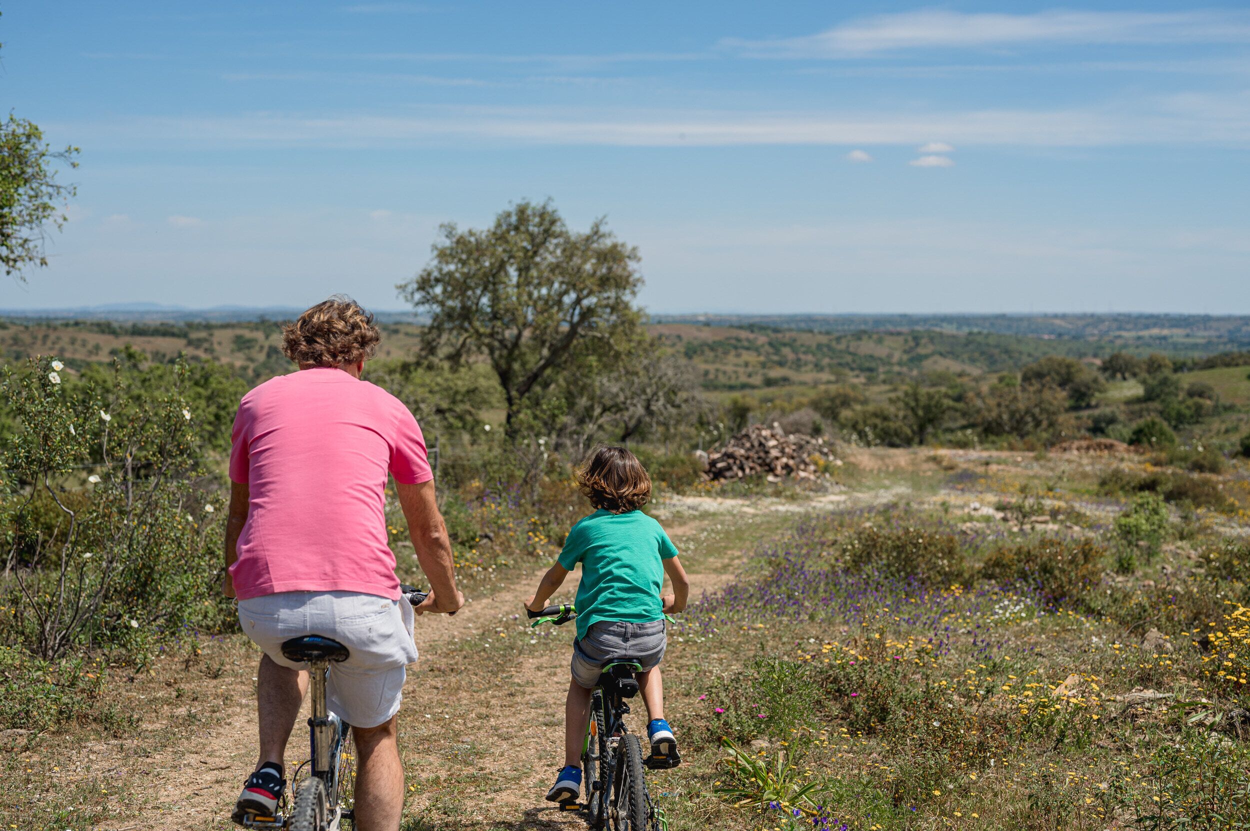 A man and a child on a bicycle trail with a natural landscape in the background.