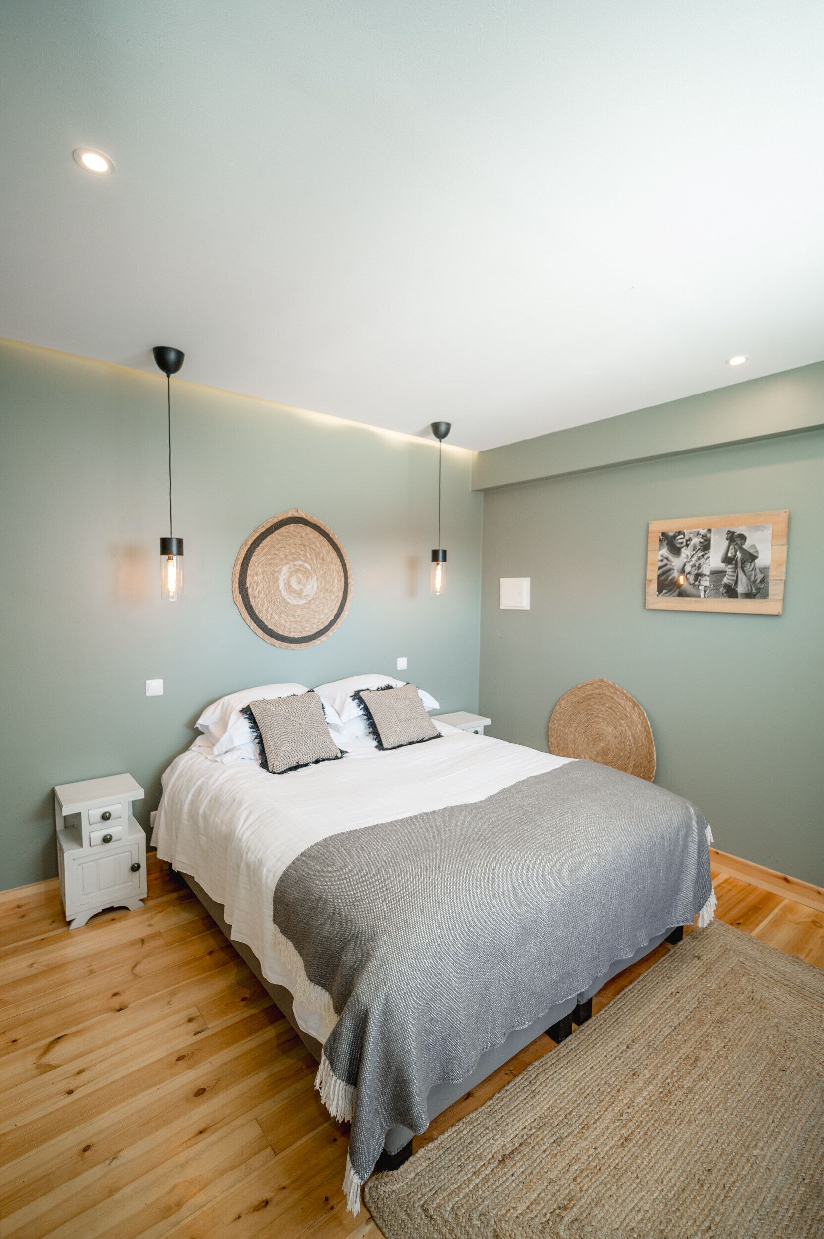 Een slaapkamer met een bed, nachtkastjes, een wandlamp, een geweven wanddecoratie en een ingelijst schilderij.