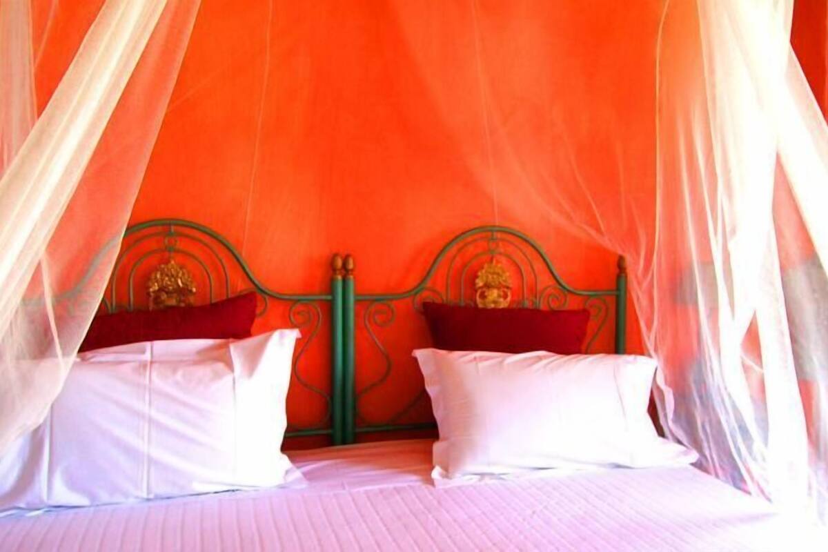 A bed with a green metal frame, white bedding, and a red pillow.