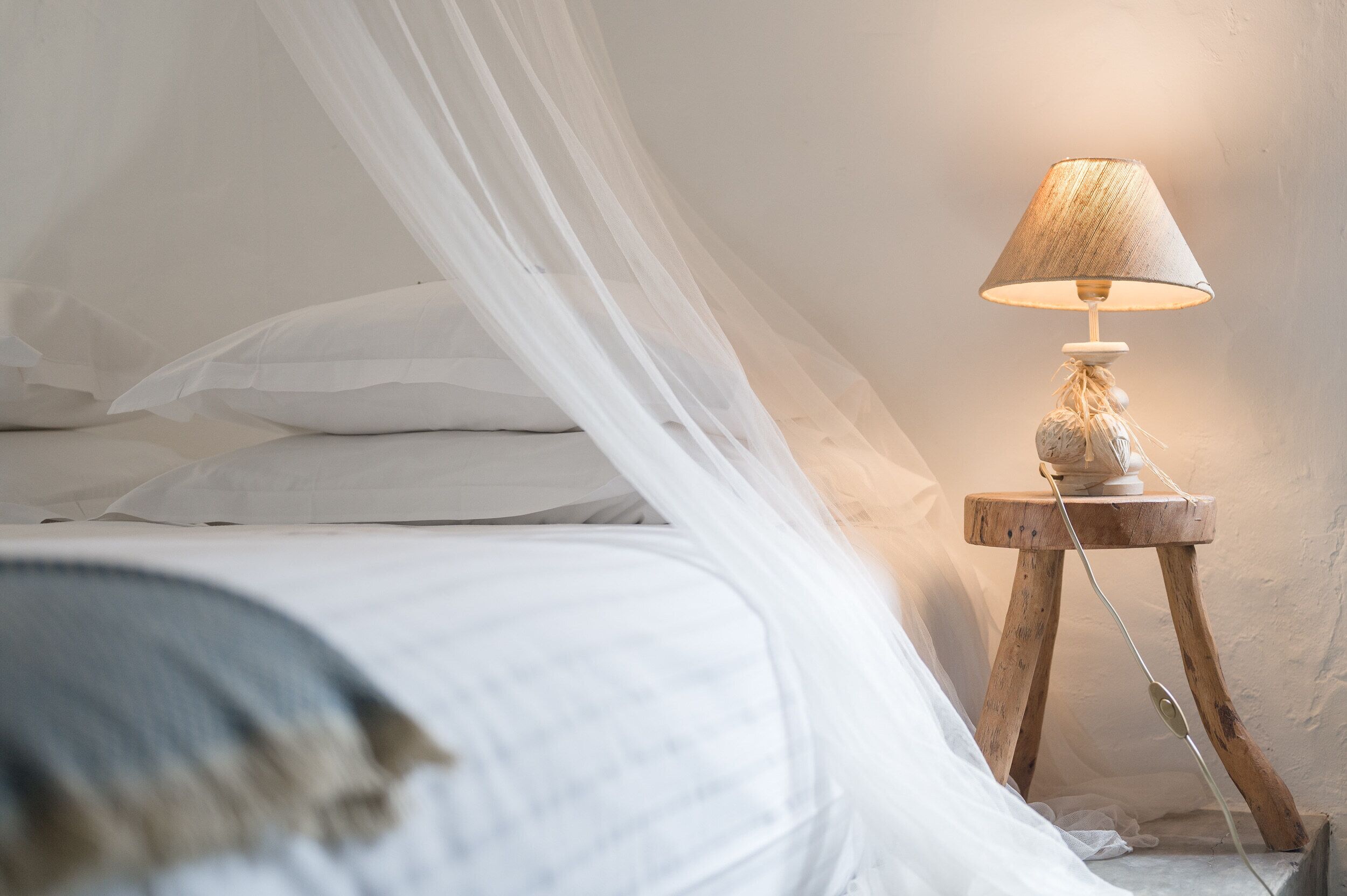 A bed with white linens and a wooden bedside table with a lamp.