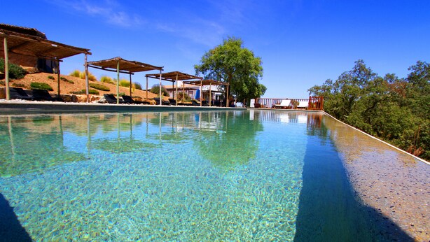 A clear swimming pool with lounge chairs and a covered seating area. - Monte Gois Country House e Spa (Almodôvar)