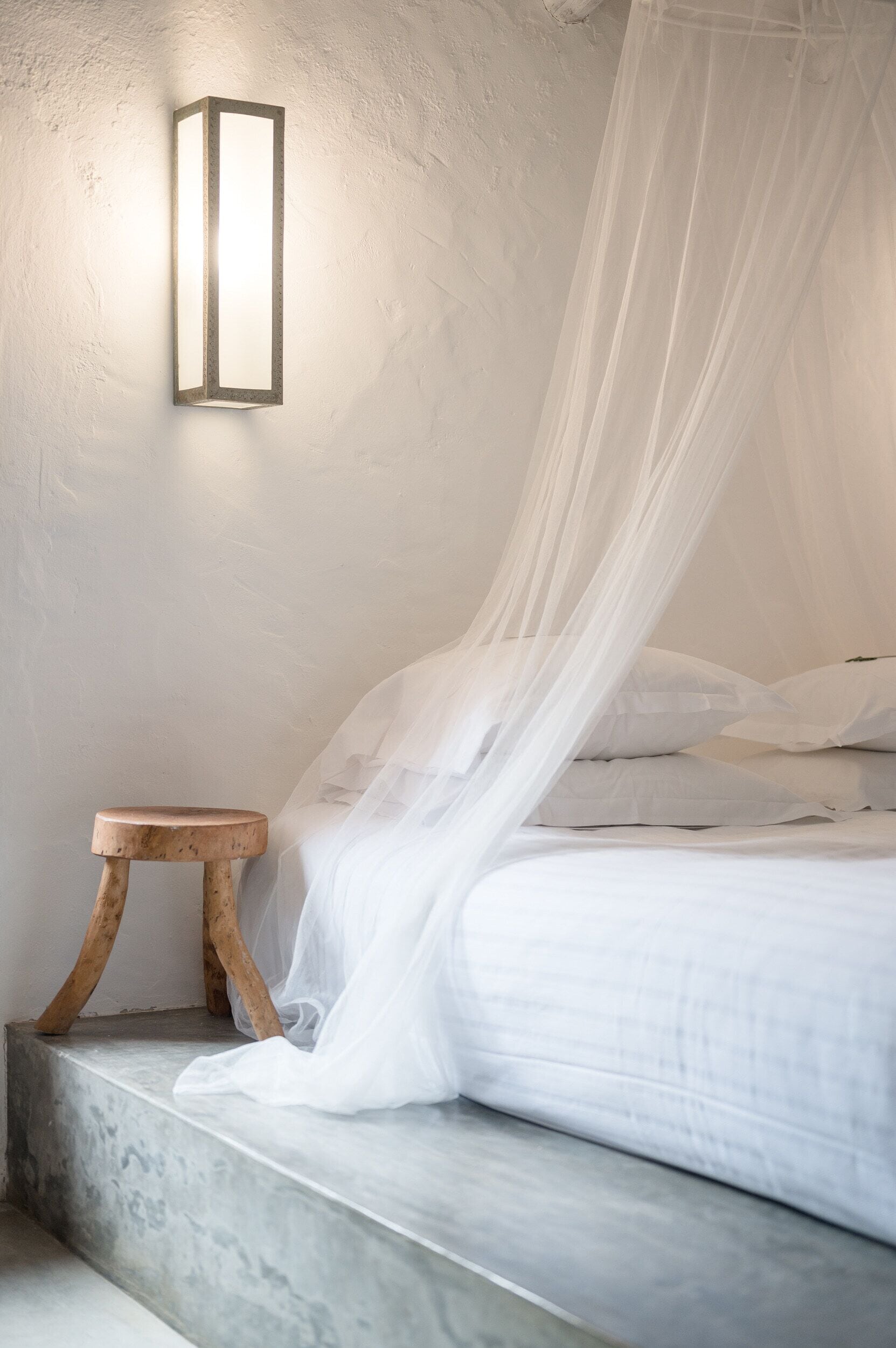 A bedroom with a bed, a bedside table, a wall-mounted light, and a canopy.