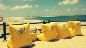 Uma praia com cadeiras infláveis amarelas com a marca 'Lipton Ice Tea' e um posto de salva-vidas.