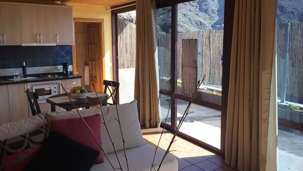 Una cocina moderna con comedor, un sofá con cojines y vistas a un paisaje montañoso a través de amplios ventanales correderas.