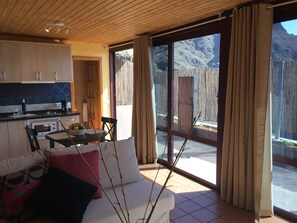 Una cocina moderna con comedor, un sofá con cojines y vistas a un paisaje montañoso a través de amplios ventanales correderas.
