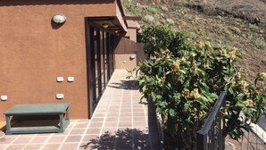 Un edificio con un patio empedrado, una banca y vistas a un paisaje montañoso.
