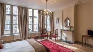 A hotel room with a large bed, a red patterned rug, a chandelier, a fireplace, and a view of the city through large windows. - Braamberg Bed & Breakfast (Bruges)