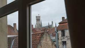 A view through a window of a building with a brick facade, a tower with a spire, and a red-tiled roof. - Braamberg Bed & Breakfast (Bruges)