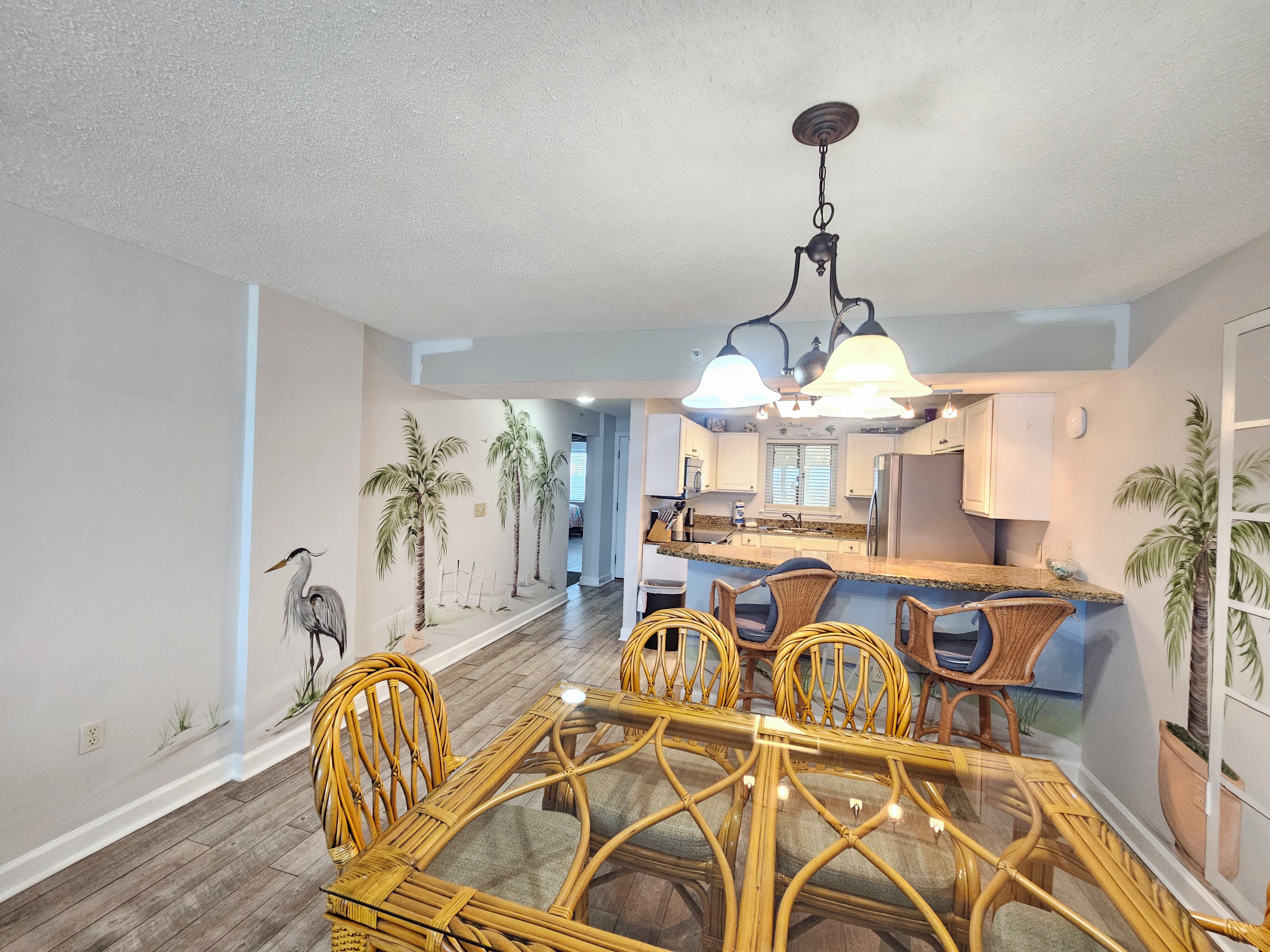 A dining area with a round table and chairs, a kitchen in the background, and a ceiling light fixture.