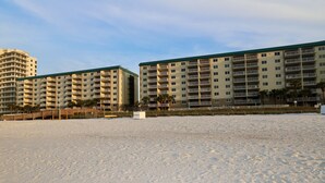 Un hotel frente a la playa con varios balcones, una playa de arena y cielo despejado.
