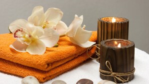 A stack of orange towels, a lit candle, and white stones on a white surface. - Flair Hotel zur Therme (Erwitte)