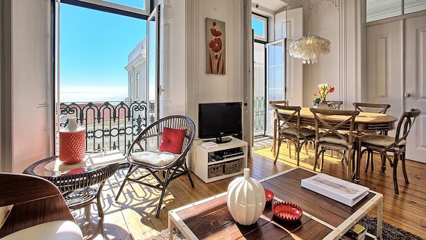 Un salon spacieux avec balcon, un plancher en bois, un coin repas avec une table et des chaises, un téléviseur et un vase décoratif.