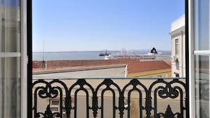 Une vue depuis un balcon doté d’une balustrade, donnant sur un port avec des navires et un ciel dégagé.