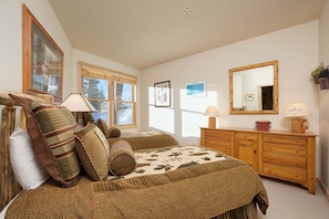 Cozy retreat with a large bed, dresser, and nightstand, surrounded by framed pictures and a potted plant.