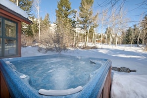 Relax in a hot tub surrounded by serene winter scenery and a mountain backdrop.