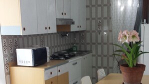 Una cocina con microondas, estufa y alacenas. Hay una mesa de comedor con sillas y una planta en maceta.