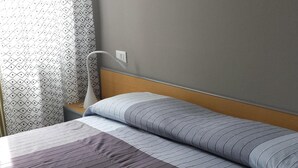 Una cama bien hecha con ropa de cama a rayas, una pared gris con dos cuadros enmarcados y una ventana con cortinas estampadas.