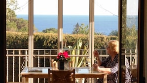 Una mujer sentada a una mesa con vista al mar a través de amplias ventanas.