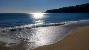 Una playa con cielos despejados y el sol reflejándose en el agua.