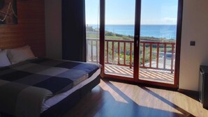 Un dormitorio con cama, suelo de madera, balcón con vistas al mar y puerta corrediza de cristal.
