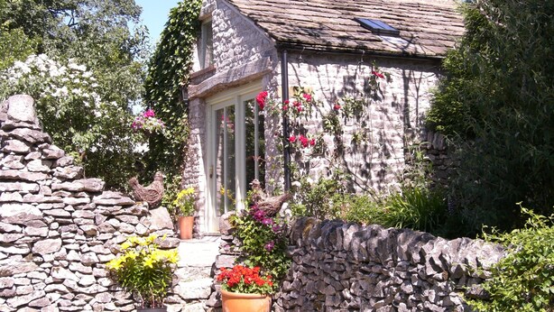 A stone cottage with a sloped roof, a door, and a small window. There are potted plants and flowers around the cottage. - Stylish cottage for 2 guests, pet friendly, dining pub nearby, Chatsworth 10m.   (Chelmorton)