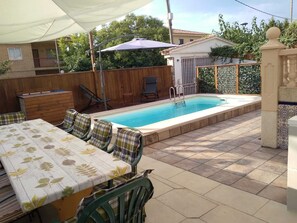 Un jardin avec une piscine, un patio couvert et une table à manger avec des chaises.
