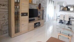 A modern living room with a wooden cabinet, TV, and glass dining table.