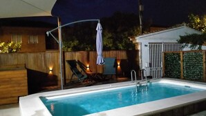 An outdoor swimming pool with a wooden deck, lounge chairs, and a covered seating area.