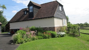 A single-story house with a sloped roof, a chimney, and a small garden with various plants and flowers.
