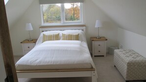 A bedroom with a large bed, two bedside tables, a window, and a bench.