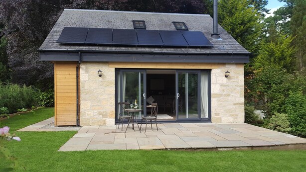 Een modern huis met een stenen gevel, grote schuifpuien en een terras met tuinmeubels.