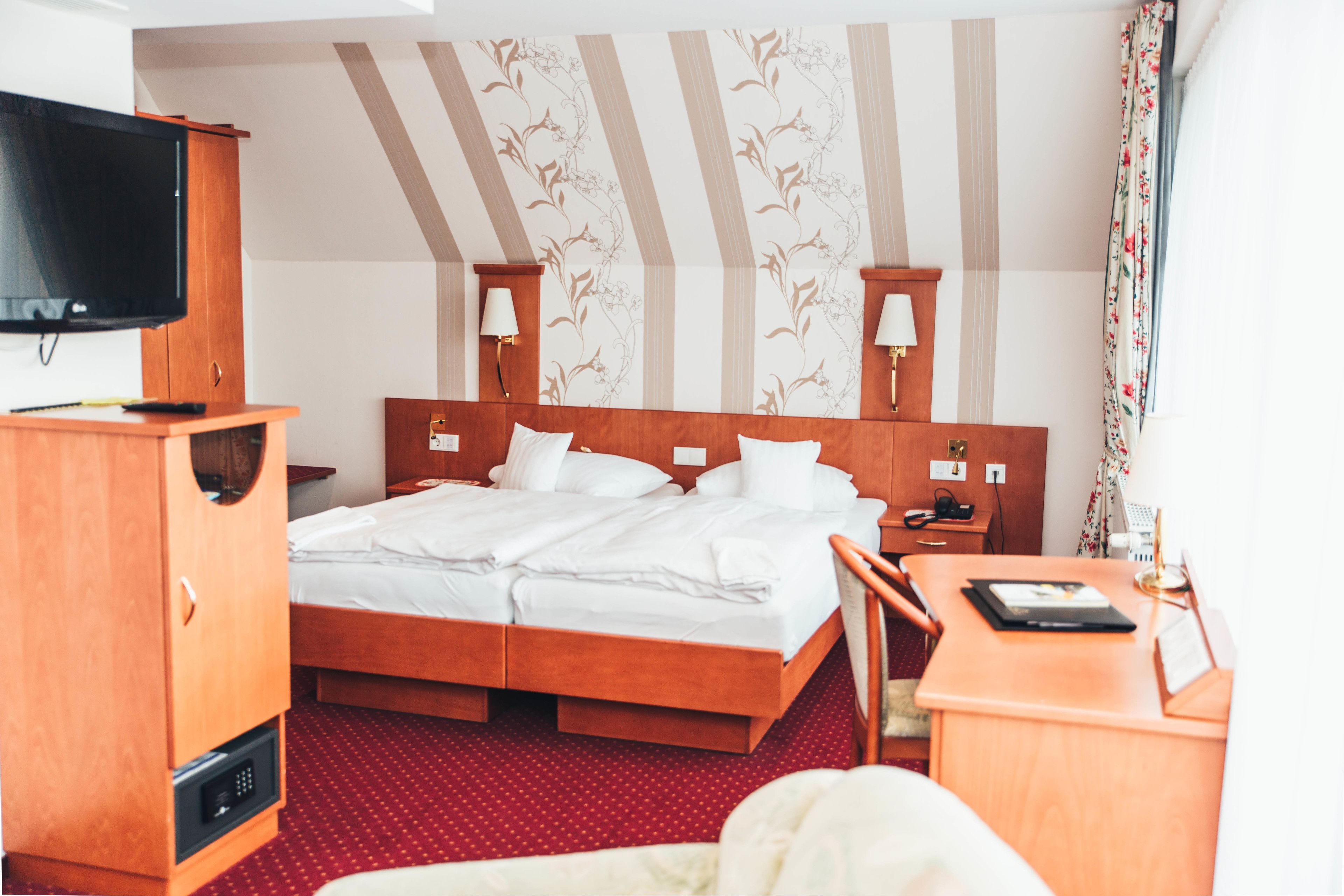 A hotel room with a bed, a desk, a television, and a wardrobe.