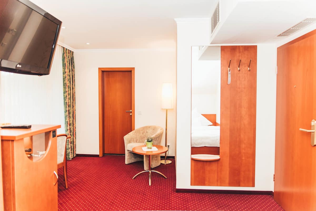 Une chambre d’hôtel équipée d’une télévision, d’une chaise, d’une petite table, d’un lit et d’une armoire.