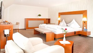A hotel room with a large bed, bedside tables, a desk, a chair, and a small plant. - Ringhotel Teutoburger Wald (Tecklenburg)