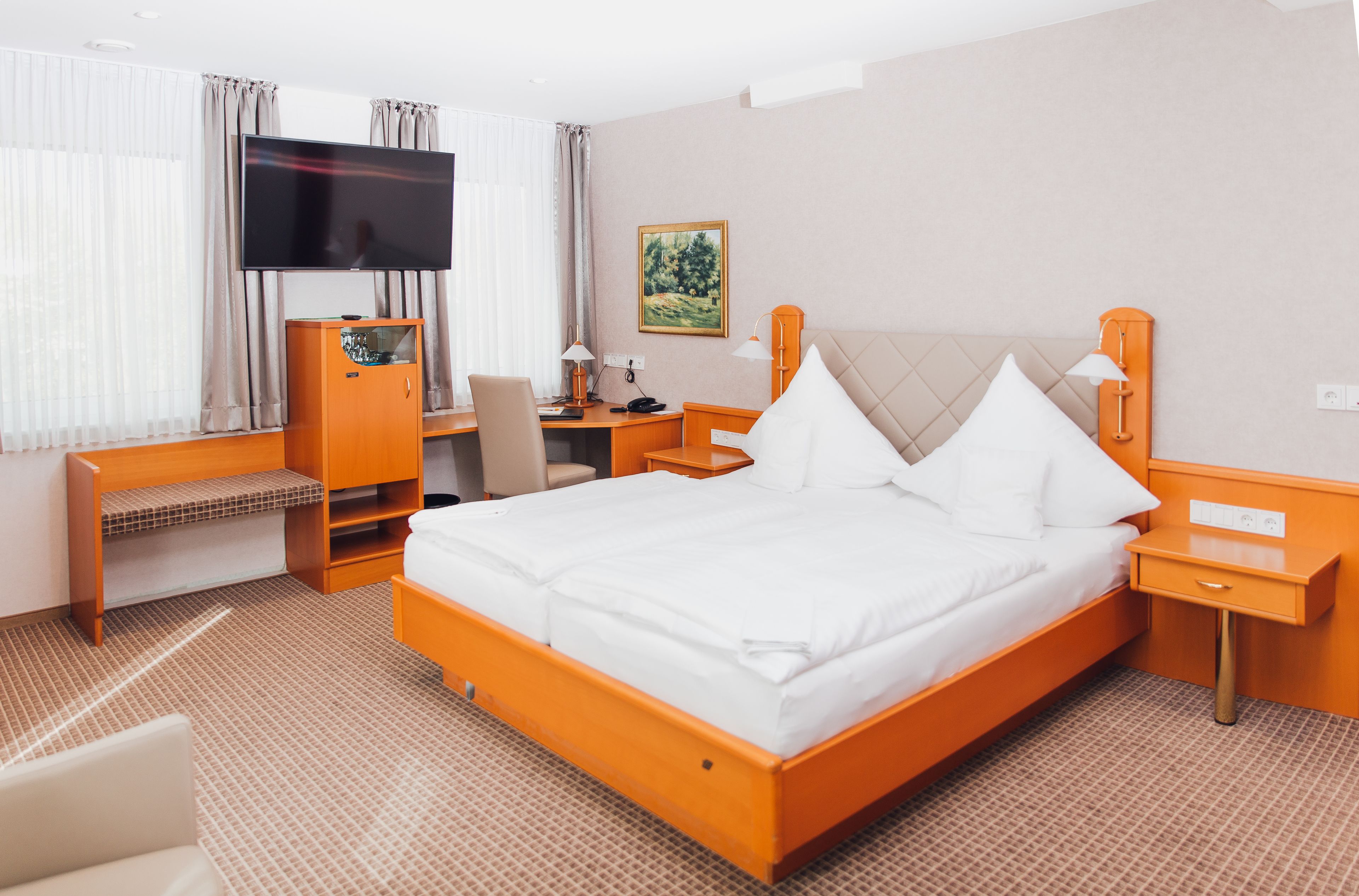 A hotel room with a large bed, a desk, a TV, and a painting on the wall.