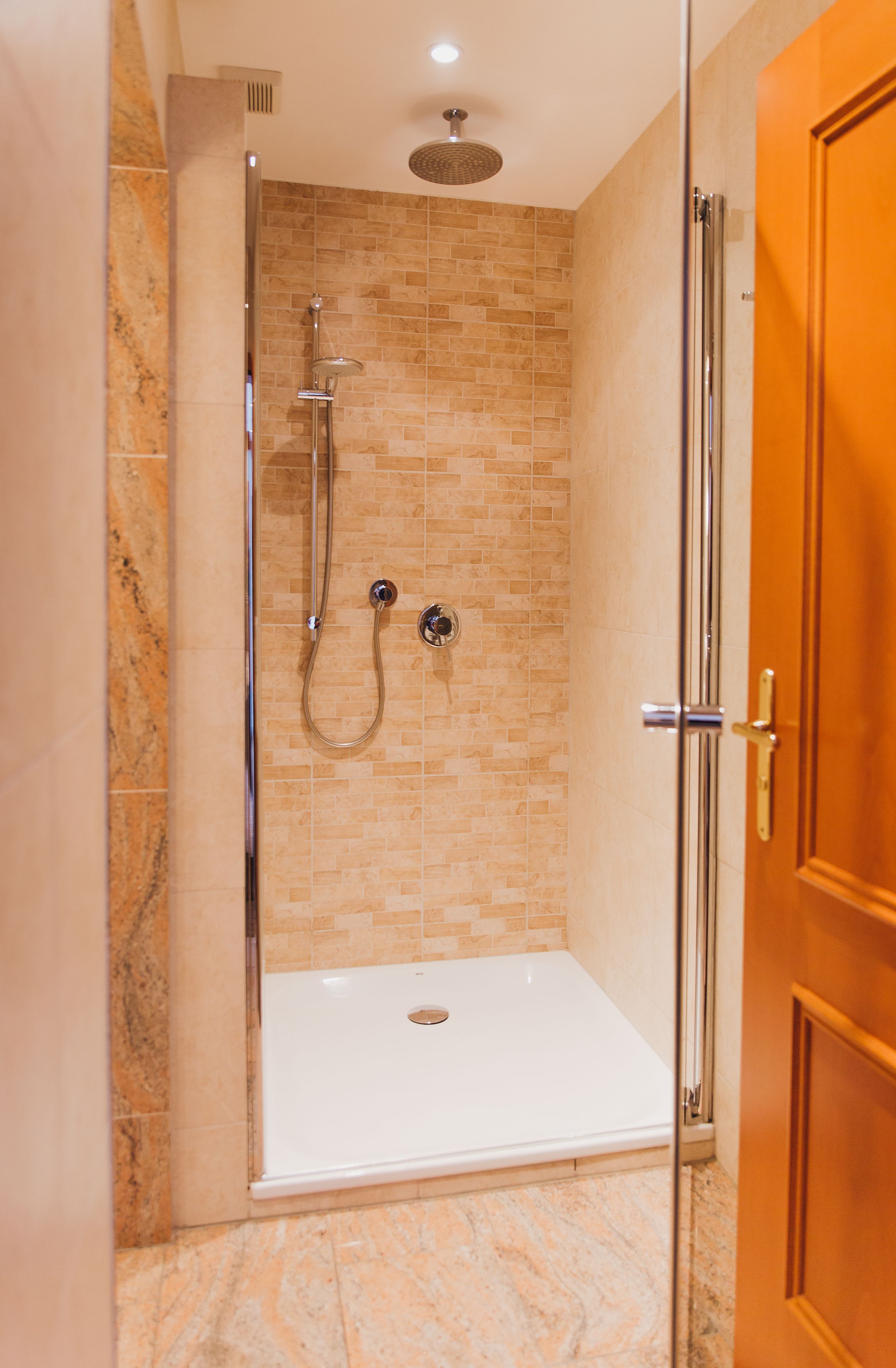 A walk-in shower with a glass door, a showerhead, and a handheld shower attachment.