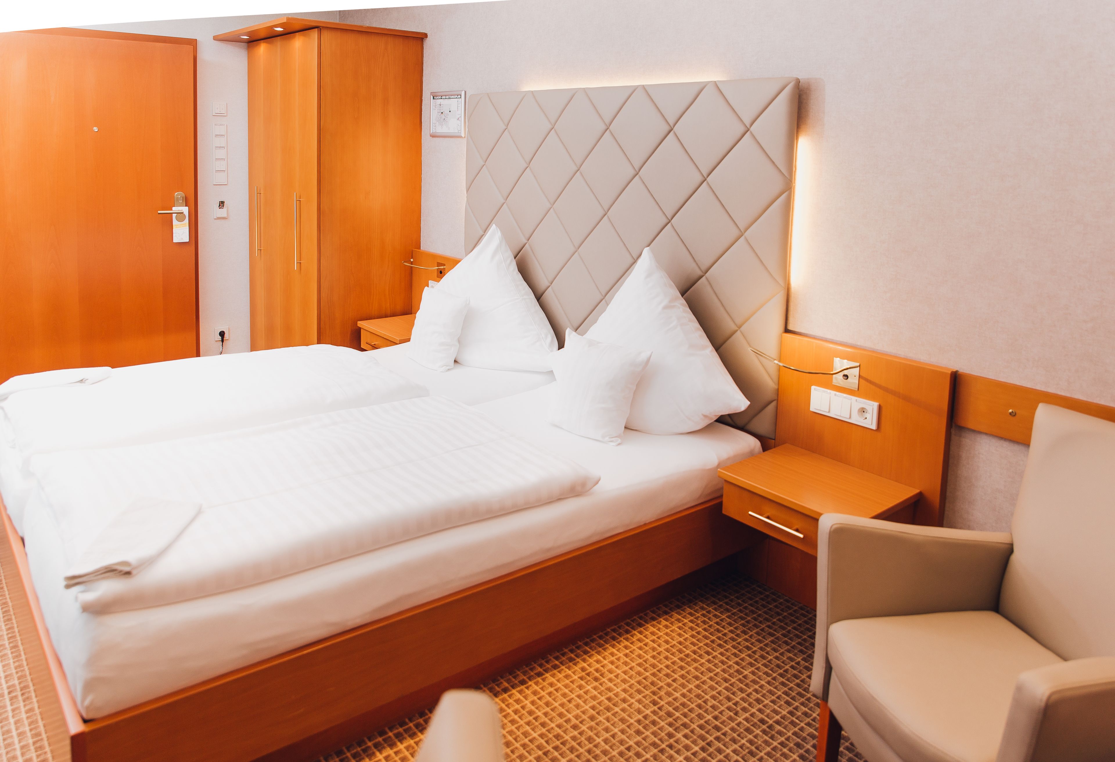 Quarto de hotel com uma cama grande, guarda-roupa de madeira, mesa de cabeceira e uma cadeira.